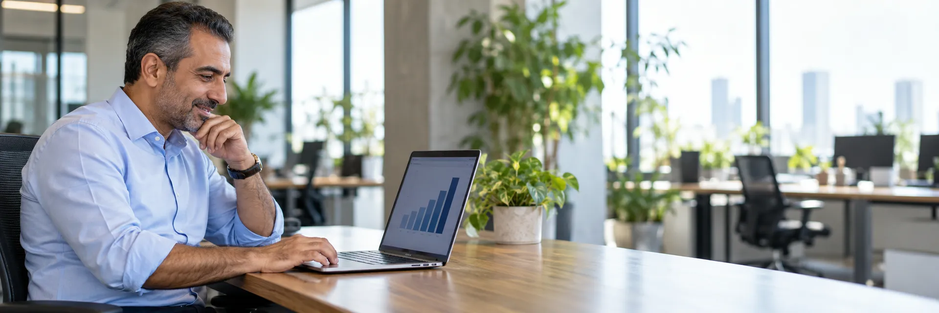 Gestionnaire RH souriant devant un graphique de progression sur son ordinateur portable, dans un bureau lumineux à aire ouverte